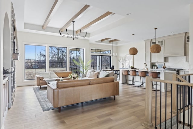 living room featuring beamed ceiling, light wood-type flooring, sink, and an inviting chandelier