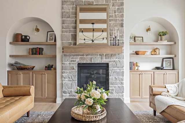 living room with a stone fireplace, light hardwood / wood-style flooring, and built in features