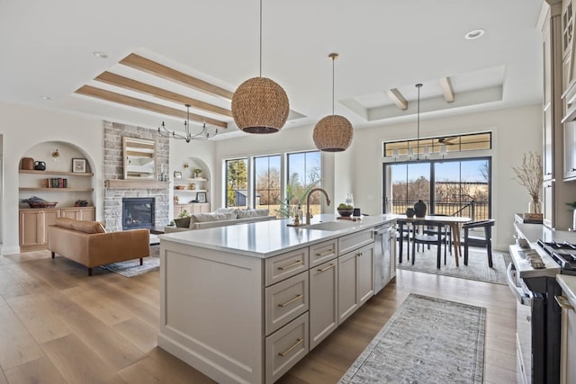 kitchen featuring stainless steel appliances, a tray ceiling, sink, a center island with sink, and hanging light fixtures