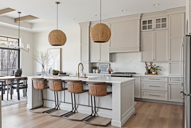 kitchen with a center island with sink, light wood-type flooring, decorative light fixtures, a kitchen bar, and custom range hood