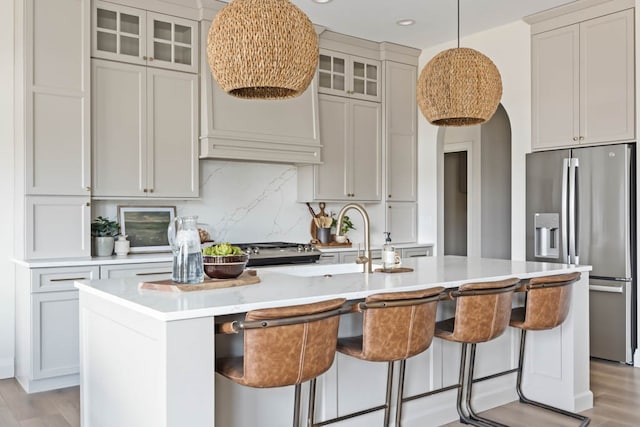 kitchen featuring stainless steel fridge, decorative light fixtures, decorative backsplash, a center island with sink, and light wood-type flooring