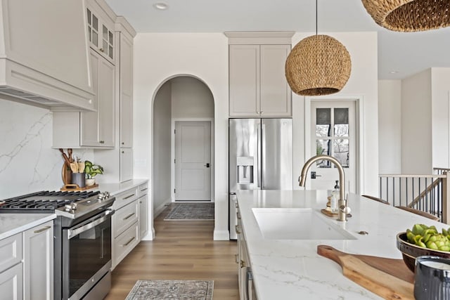 kitchen with light stone countertops, sink, dark hardwood / wood-style floors, decorative light fixtures, and appliances with stainless steel finishes