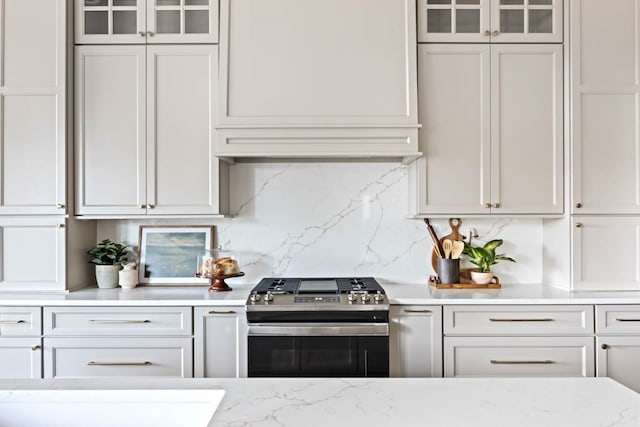 kitchen with backsplash, light stone counters, white cabinetry, and stainless steel range with gas stovetop