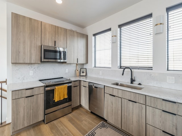 kitchen featuring light stone counters, light wood-style flooring, a sink, stainless steel appliances, and tasteful backsplash