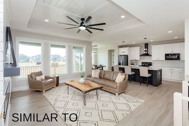 living room featuring light hardwood / wood-style flooring, a tray ceiling, and ceiling fan with notable chandelier