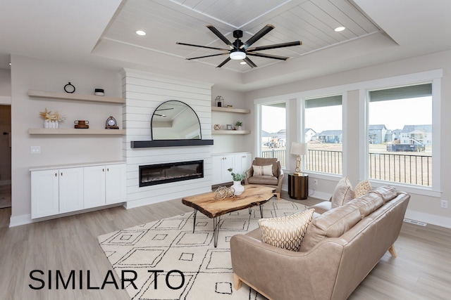 living room featuring wood ceiling, light hardwood / wood-style flooring, a large fireplace, a raised ceiling, and ceiling fan