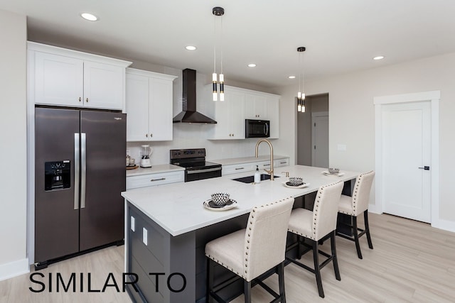 kitchen featuring a kitchen island with sink, black appliances, sink, wall chimney exhaust hood, and decorative light fixtures