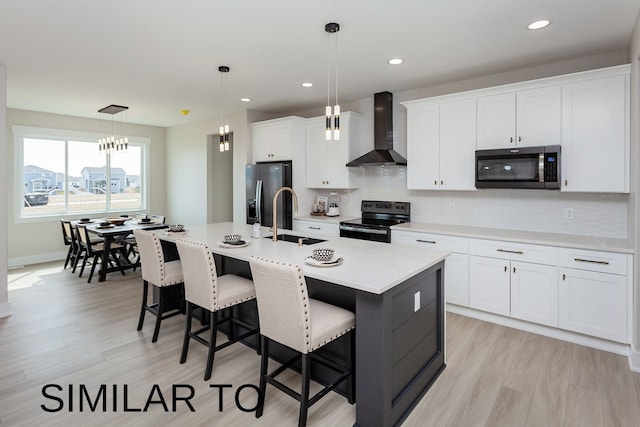 kitchen featuring wall chimney range hood, an island with sink, sink, pendant lighting, and stainless steel appliances