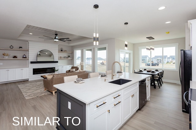 kitchen with a center island with sink, white cabinetry, black appliances, pendant lighting, and sink