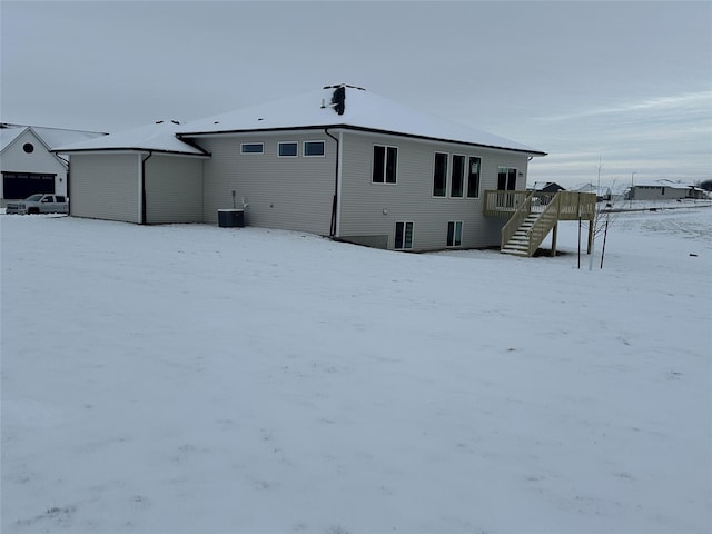 snow covered rear of property with central AC and a deck