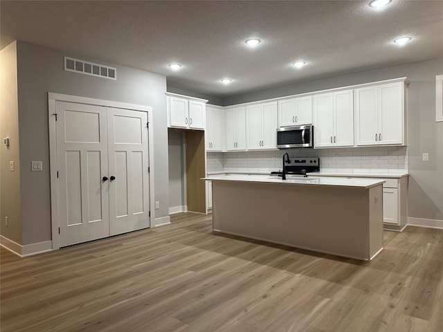 kitchen with an island with sink, light hardwood / wood-style flooring, white cabinets, and stainless steel appliances