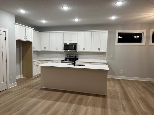 kitchen with backsplash, an island with sink, light hardwood / wood-style floors, white cabinets, and appliances with stainless steel finishes