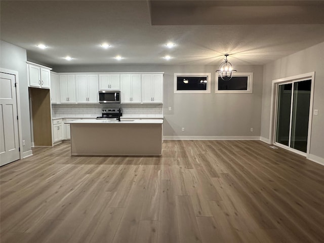 kitchen with a center island with sink, appliances with stainless steel finishes, tasteful backsplash, white cabinetry, and a chandelier