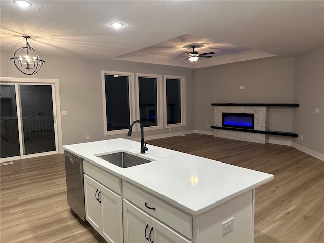 kitchen with a center island with sink, a raised ceiling, stainless steel dishwasher, and sink