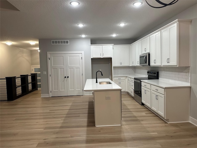 kitchen featuring stainless steel appliances, decorative backsplash, a center island with sink, white cabinets, and light wood-type flooring