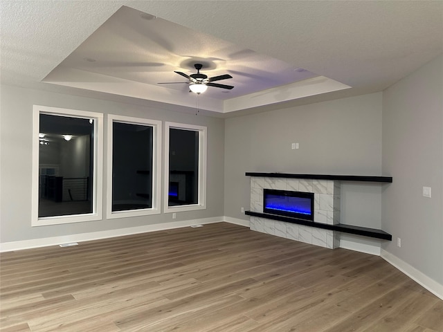 unfurnished living room featuring hardwood / wood-style floors, ceiling fan, a fireplace, and a tray ceiling