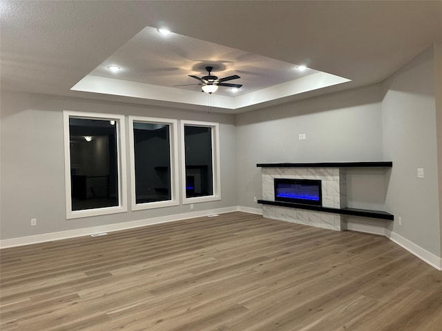 unfurnished living room with hardwood / wood-style floors, a tile fireplace, a raised ceiling, ceiling fan, and a textured ceiling