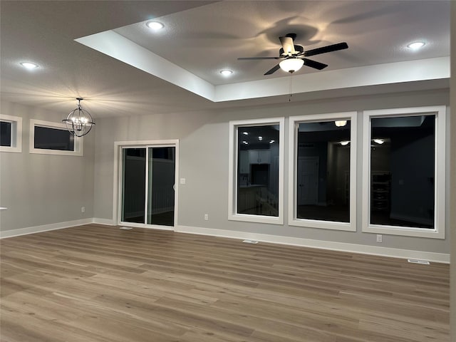 empty room with wood-type flooring, ceiling fan with notable chandelier, and a tray ceiling