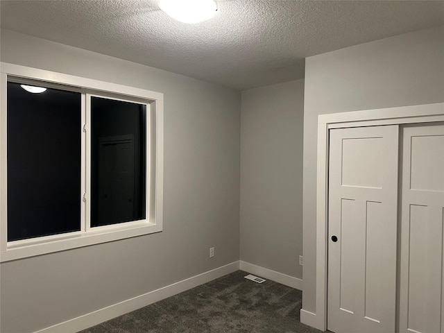 spare room with a textured ceiling and dark carpet