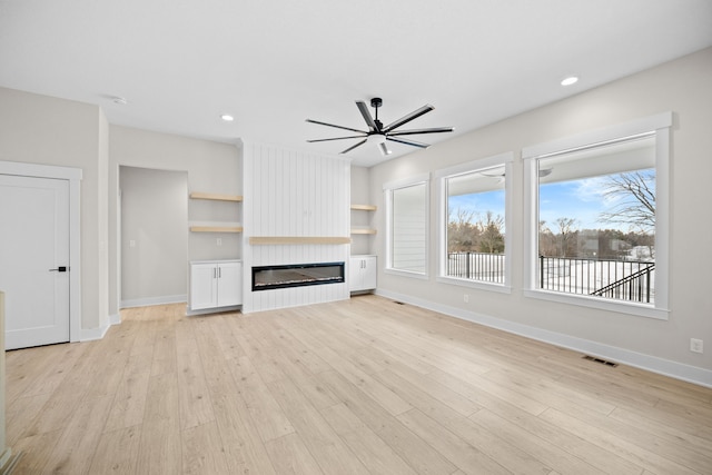 unfurnished living room with light hardwood / wood-style floors, a large fireplace, built in features, and a wealth of natural light