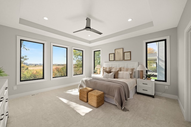 bedroom featuring ceiling fan, a raised ceiling, light colored carpet, and multiple windows