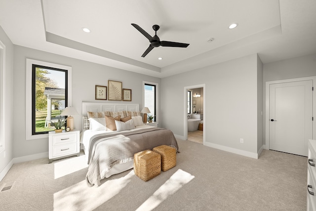 bedroom with light carpet, a raised ceiling, ensuite bath, and ceiling fan