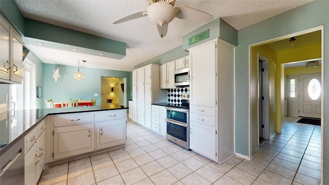 kitchen with appliances with stainless steel finishes, dark countertops, a peninsula, and light tile patterned floors