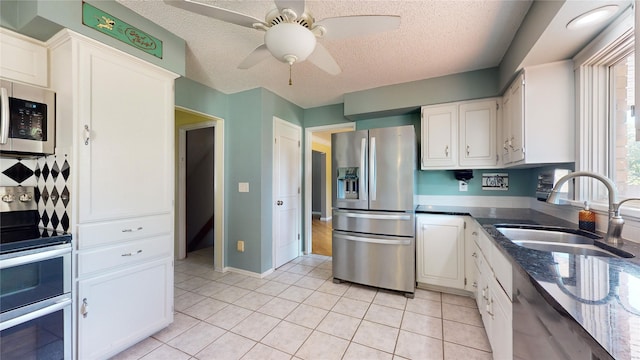 kitchen with light tile patterned floors, a textured ceiling, stainless steel appliances, a sink, and white cabinets