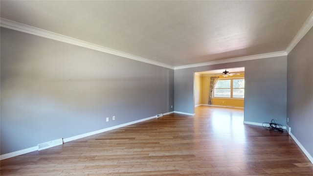 empty room with wood finished floors, a ceiling fan, visible vents, baseboards, and ornamental molding