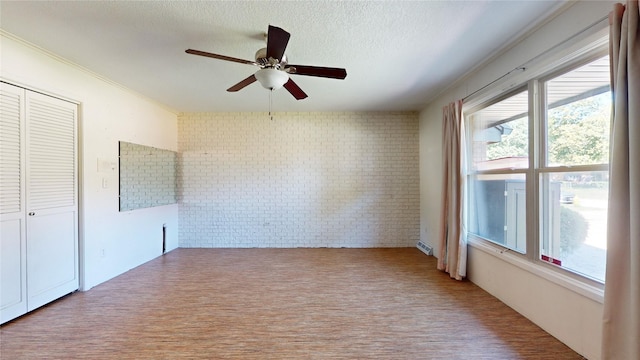 empty room with a textured ceiling, brick wall, wood finished floors, and a ceiling fan