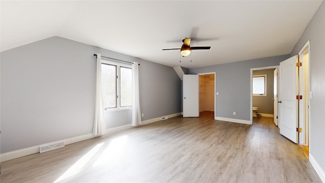 unfurnished bedroom featuring a walk in closet, lofted ceiling, visible vents, light wood-style floors, and baseboards