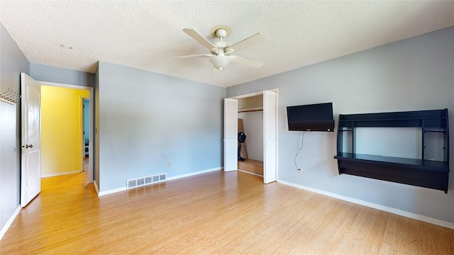 unfurnished living room with ceiling fan, a textured ceiling, wood finished floors, visible vents, and baseboards