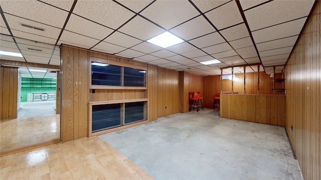 finished below grade area with a paneled ceiling, wooden walls, and visible vents