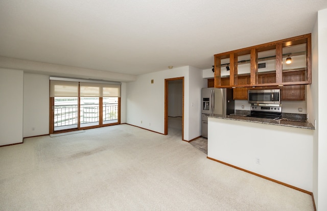 kitchen featuring appliances with stainless steel finishes, kitchen peninsula, dark stone countertops, and light carpet