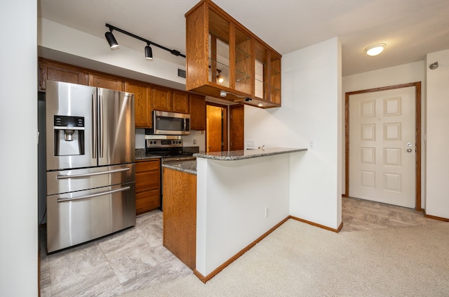 kitchen featuring appliances with stainless steel finishes, light colored carpet, dark stone counters, kitchen peninsula, and rail lighting