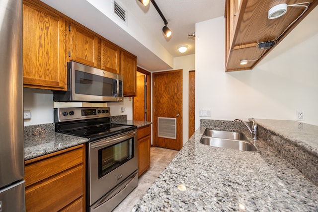 kitchen with a textured ceiling, light stone counters, sink, and appliances with stainless steel finishes