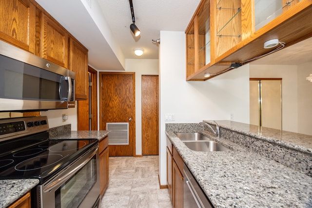 kitchen with a textured ceiling, light stone counters, stainless steel appliances, and sink