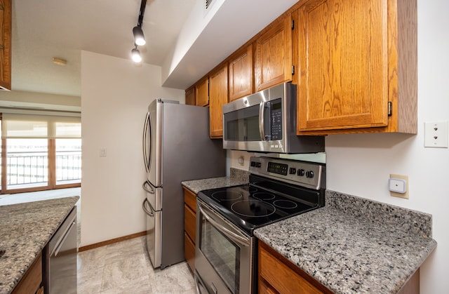 kitchen with track lighting, appliances with stainless steel finishes, and light stone countertops