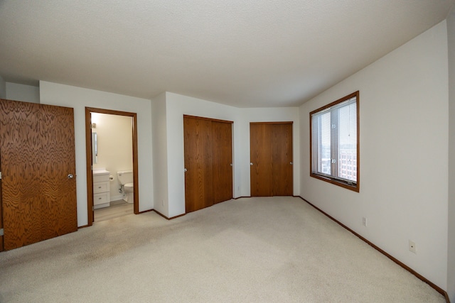 unfurnished bedroom with a textured ceiling, light colored carpet, and ensuite bathroom