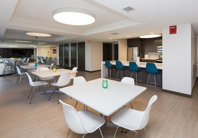 dining space with light wood-type flooring and a raised ceiling