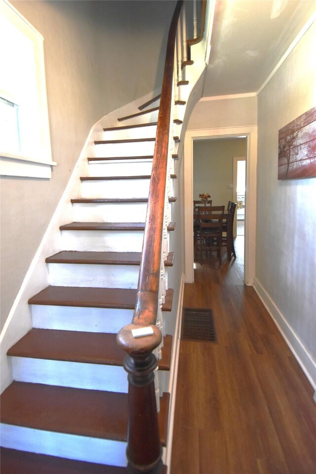 stairway with ornamental molding and wood-type flooring