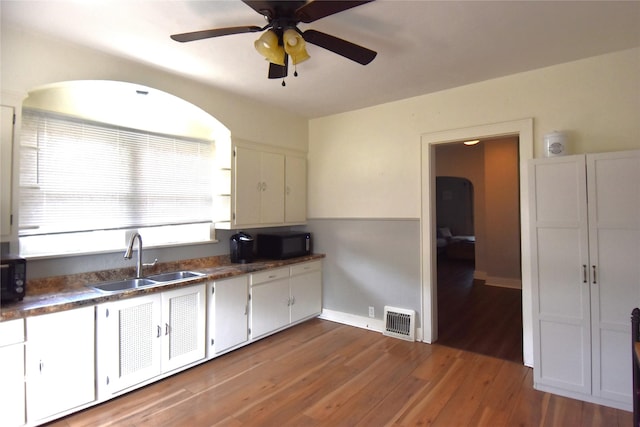 kitchen featuring wood finished floors, visible vents, a sink, black microwave, and dark countertops