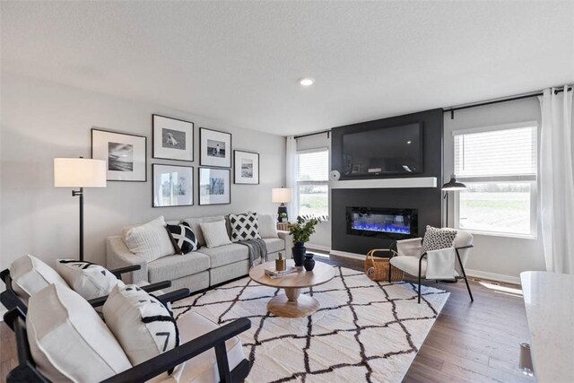 living area featuring a glass covered fireplace, recessed lighting, wood finished floors, and baseboards