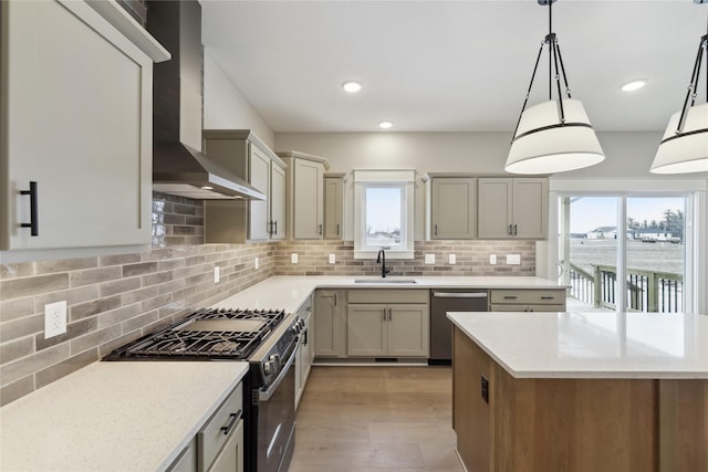 kitchen with backsplash, wall chimney range hood, sink, appliances with stainless steel finishes, and decorative light fixtures