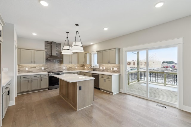 kitchen featuring wall chimney exhaust hood, stainless steel appliances, decorative light fixtures, light hardwood / wood-style flooring, and a kitchen island