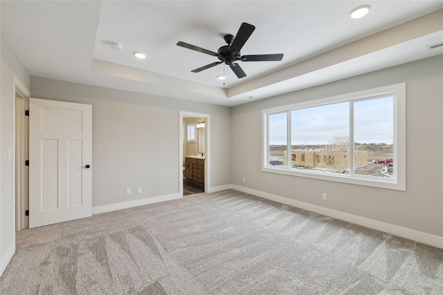 unfurnished bedroom featuring ceiling fan, light carpet, connected bathroom, and a tray ceiling