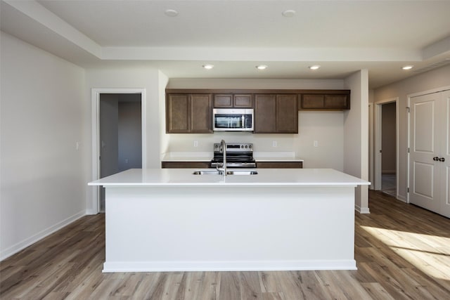 kitchen featuring stainless steel appliances, sink, light hardwood / wood-style floors, and a center island with sink