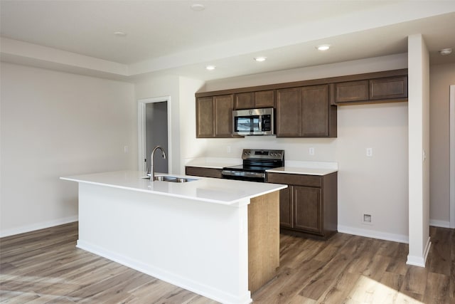 kitchen featuring dark brown cabinetry, sink, an island with sink, stainless steel appliances, and light hardwood / wood-style floors