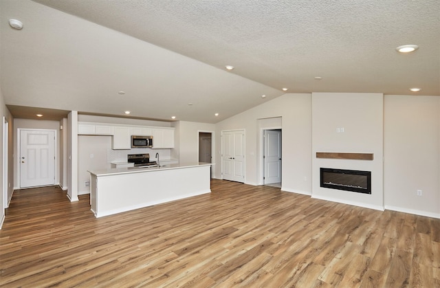 unfurnished living room with sink, light wood-type flooring, a textured ceiling, and vaulted ceiling