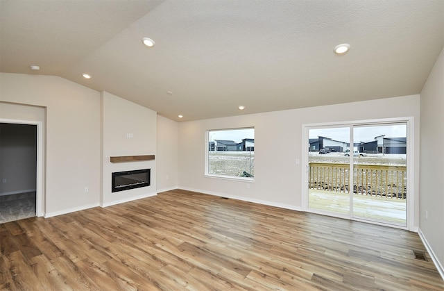 unfurnished living room featuring a textured ceiling, vaulted ceiling, and light hardwood / wood-style flooring